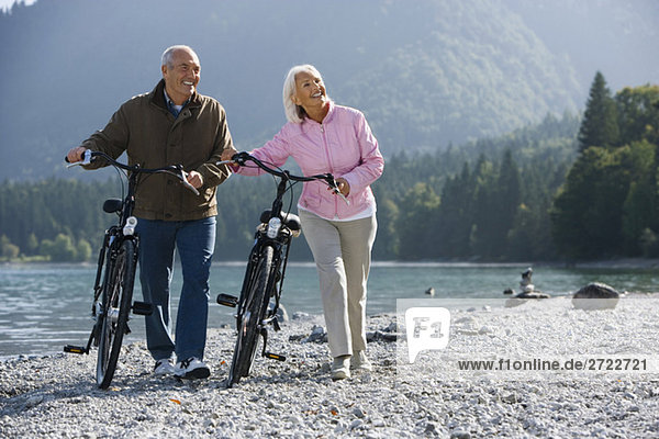 Germany  Bavaria  Walchensee  Senior couple pushing bikes across lakeshore