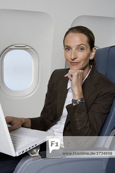 Eine Geschäftsfrau  die an einem Laptop im Flugzeug arbeitet.