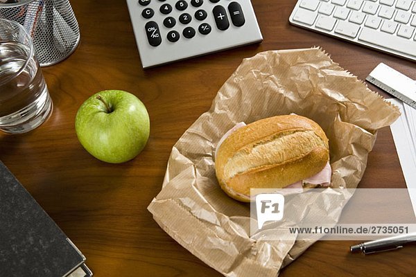 Ein Schreibtisch mit Büromaterial und einem Sandwich und einem Apfel darauf.
