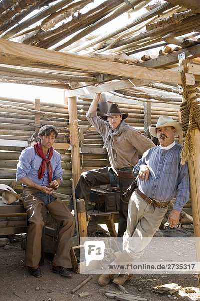 Drei Cowboys stehen in einem Holzschuppen.