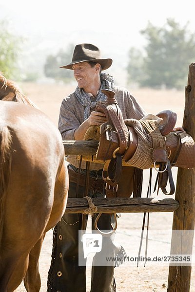 Ein Rancher  der einen Pferdesattel auf einem Zaun vorbereitet.