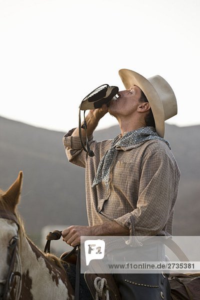 Ein Cowboy sitzt auf einem Pferd und trinkt aus einem Flachmann.