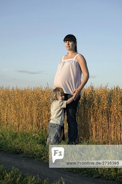 A pregnant woman and her young boy standing near a wheat field