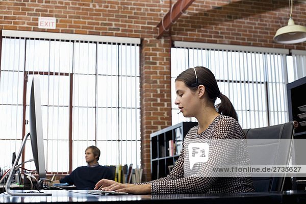 Eine Frau  die ein Headset trägt und einen Computer in einem Büro benutzt.
