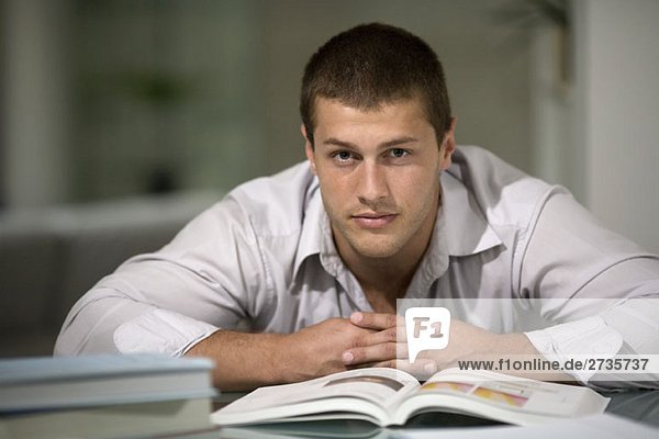 A young man leaning on a desk with an open book