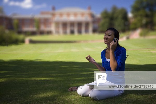Eine junge Frau  die ein Handy auf dem Rasen der Universität benutzt.