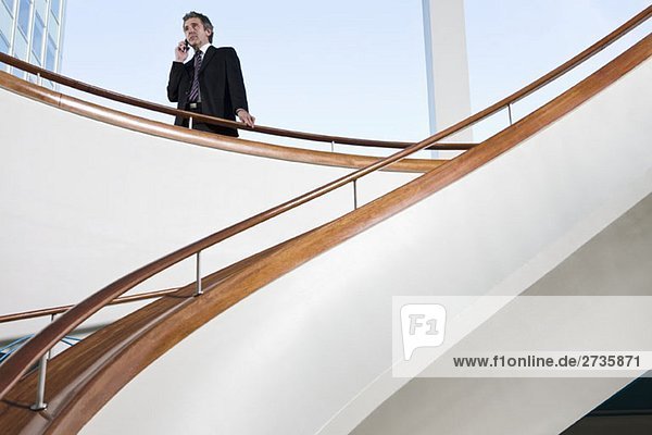 Ein Mann  der auf seinem Handy oben auf einer Treppe spricht.