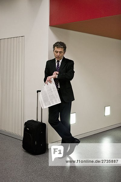 Ein Geschäftsmann  der mit seinem Koffer wartet und eine Zeitung hält.