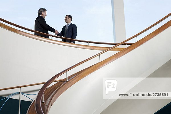 Zwei Geschäftsleute  die auf einem Balkon stehen und sich die Hand schütteln.