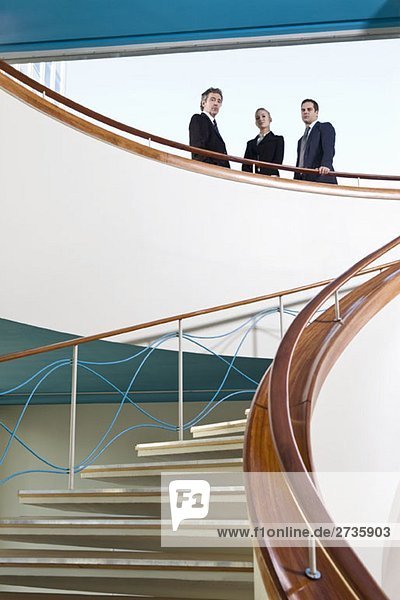 Drei Geschäftsleute  die oben auf einer Treppe stehen.