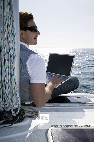 Rear view of a man using a laptop on a yacht