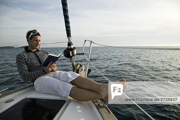 Ein Mann liest am Bug einer Yacht.