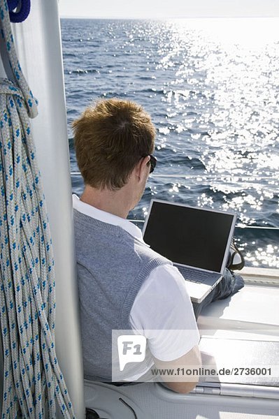 Rückansicht eines Mannes mit einem Laptop auf einer Yacht