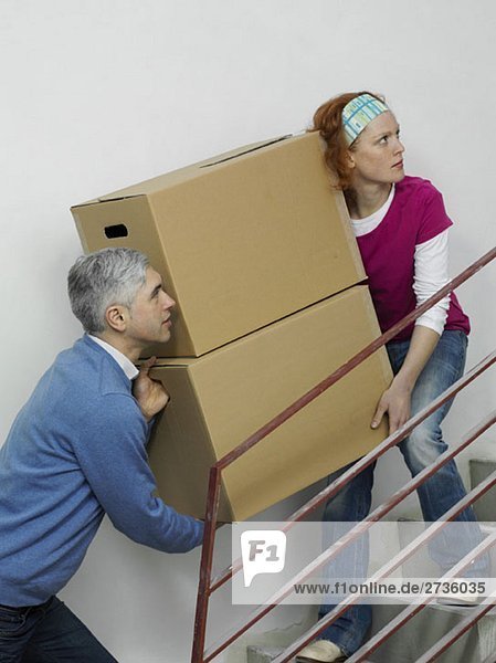 A couple carrying boxes together up stairs