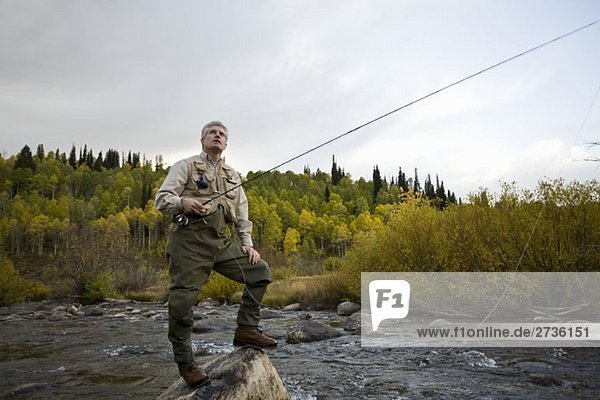 A man standing on a rock while fly fishing in a river