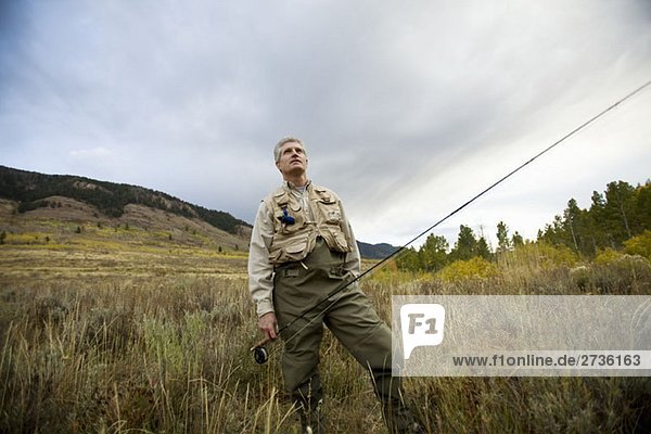 A man standing in a field with a fly rod