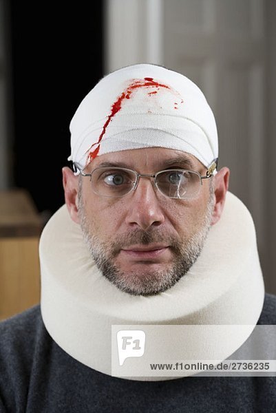 Ein Mann mit einer kaputten Brille  einem blutigen Verband am Kopf und einer Halskrause.