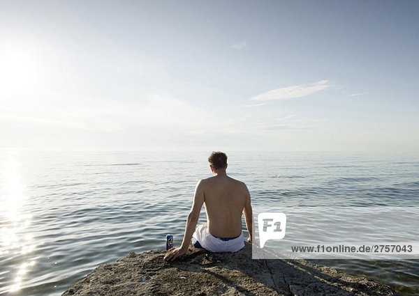 Mann sitzt auf einem Felsen am Meer