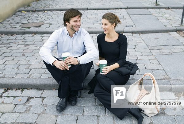 Mann und Frau sitzen auf einer Treppe und trinken Kaffee.