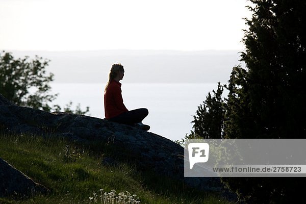 Eine Frau sitzend auf einem Felsen Granna Schweden.