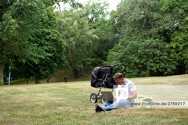 Ein Mann mit Kinderwagen und einen Laptop in einem Park am sonnigen Tag Schweden.
