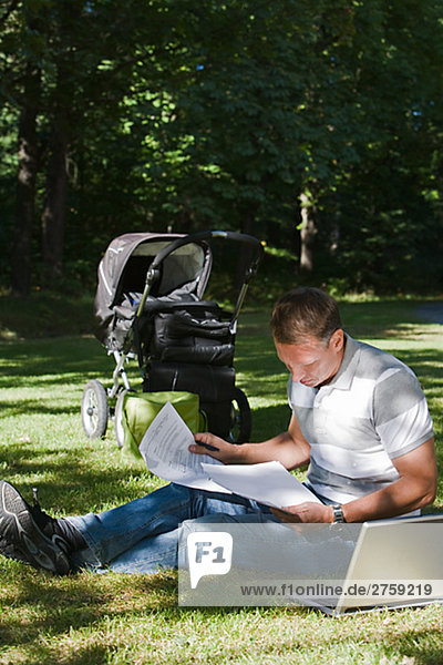 Ein Mann mit Kinderwagen und ein Computer in einem Park am sonnigen Tag Schweden.