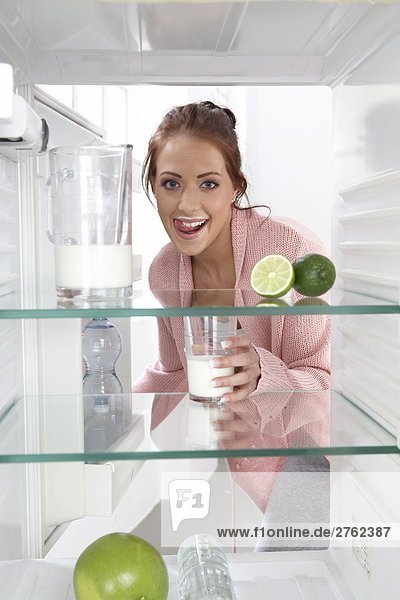 Portrait einer jungen Frau setzen Milkglass im Kühlschrank und lächelnd