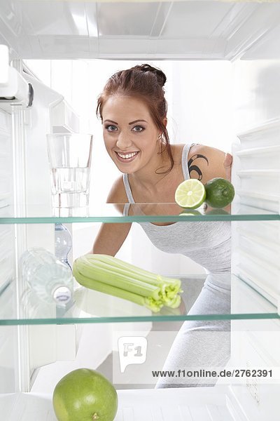 Portrait einer jungen Frau lächelnd vor Öffnen Kühlschrank