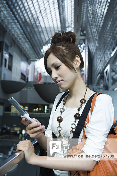 Young female text messaging on cell phone in shopping mall