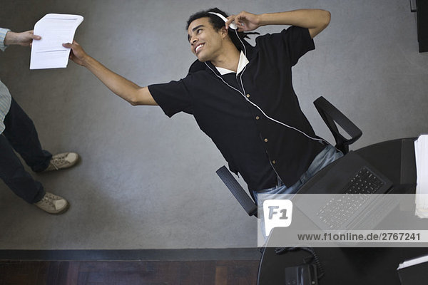 Junger Büroangestellter  der sich im Stuhl zurücklehnt  um Dokumente von einem Kollegen zu erhalten  Blick in die Höhe