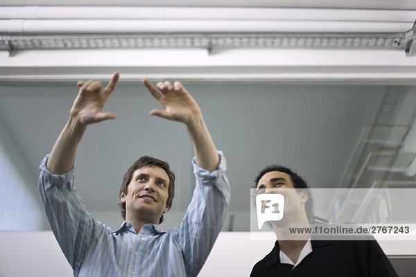 Man making gesture  explaining to colleague looking on
