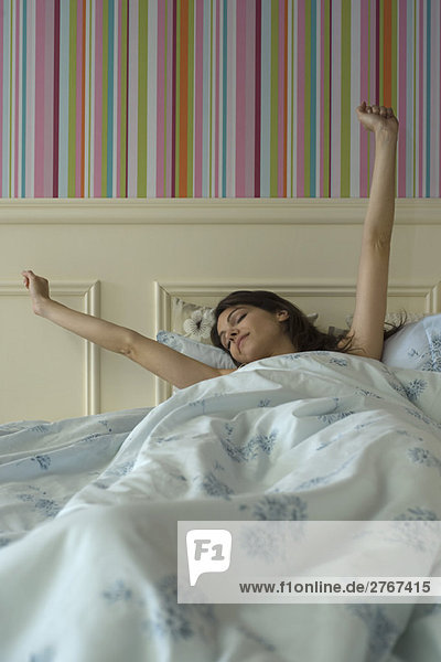 Young woman stretching in bed  arms raised