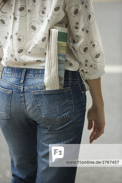 Woman with newspaper rolled up in back pocket of jeans  cropped view