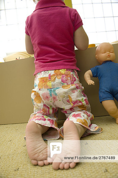 Kleines Mädchen kniend vor Spielzeugkiste  Rückansicht