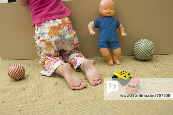 Kleines Mädchen kniend auf dem Boden mit Spielzeug  Rückansicht  beschnitten