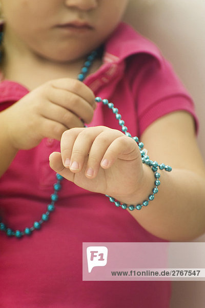 Kleines Mädchen wickelt Perlenkette um das Handgelenk  beschnitten