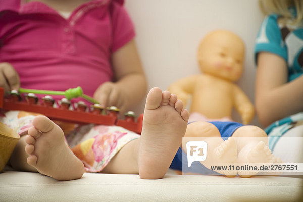 Kleines Mädchen neben Babypuppe sitzend  Nahaufnahme von nackten Füßen