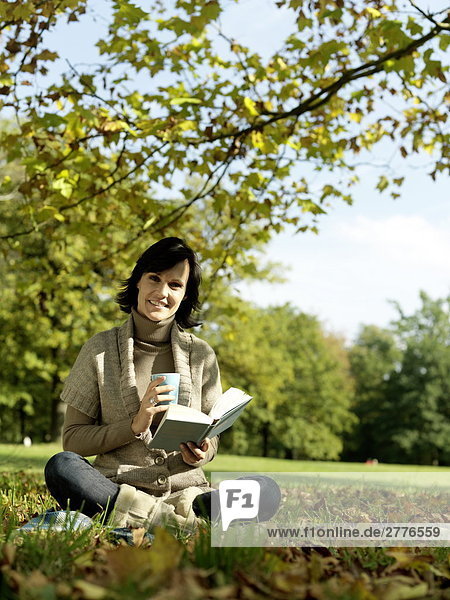 Portrait reife Frau hält Buch und lächelnd im park