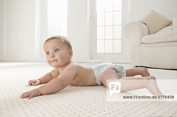 A baby lying on the lounge carpet.