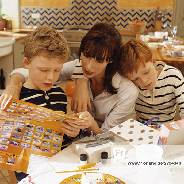 Mutter und Sohn beim Lesen von Spielzeuganleitungen nach der Geburtstagsfeier  zweiter Sohn lehnt an Mutter