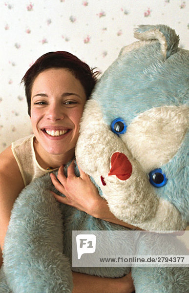 Junge Frau umarmt Teddybär lächelnd vor der Kamera