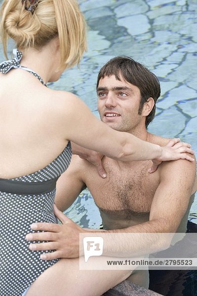 Frau sitzt am Pool  Mann steht vor ihr im Wasser