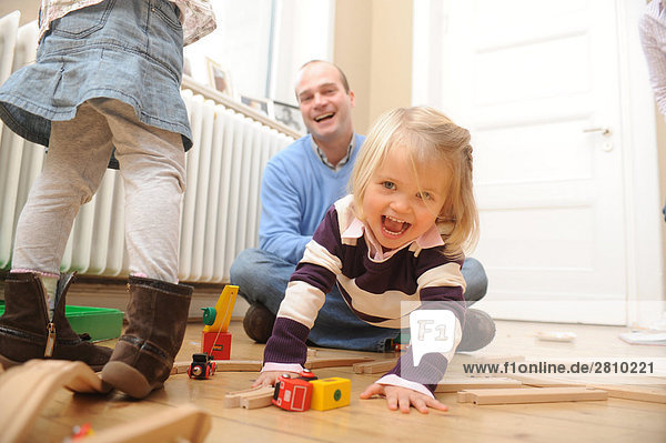Mädchen mit Spielzeug und ihrem Vater zieht spielerisch ihr spielen