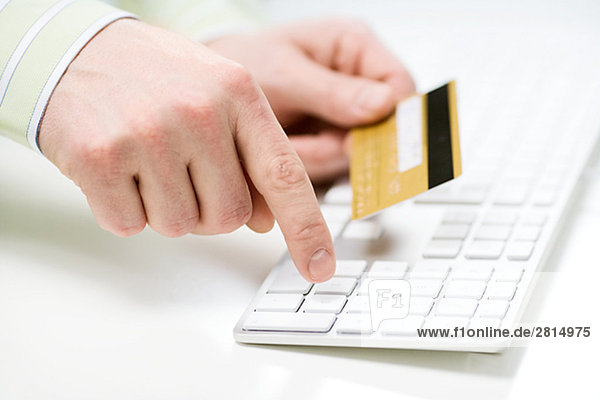 A hand holding a credit card and using a keyboard Sweden.