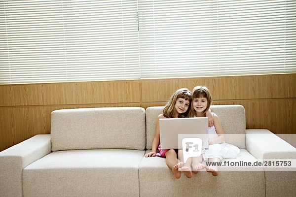 Two girls sitting in a sofa with a computer.