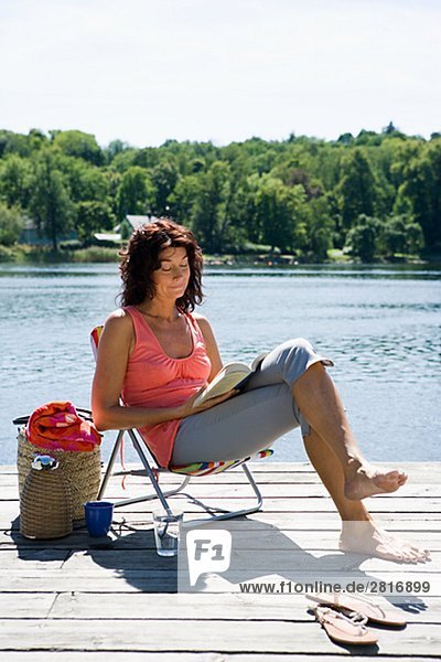 Eine Frau  lesen ein Buch über eine Mole ein See Schwedens.