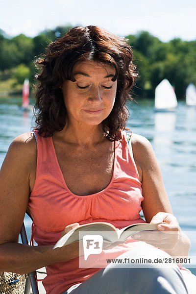 A woman reading a book on a jetty by a lake Sweden.