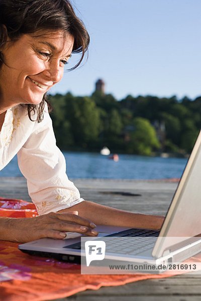 Eine Frau mit einem Laptop auf einer Mole ein See Schwedens.
