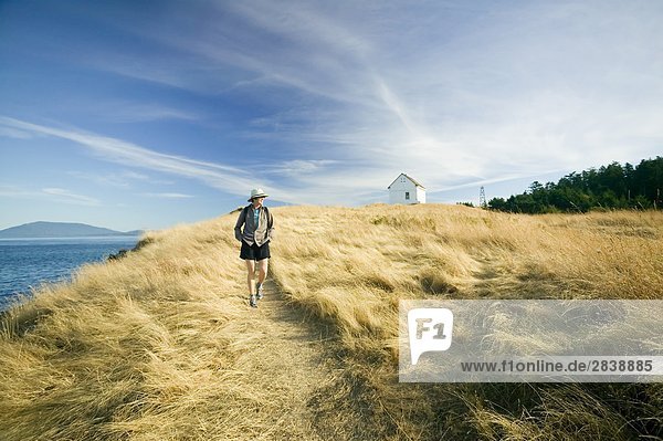 woman walking past old fog horn building at East Point Park and lighthouse  Saturna Island  British Columbia  Canada.
