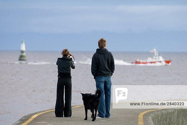 A young couple watches the Victoria BC harbour Pilot boat return to port from the Ogden Point breakwater  Victoria  Vancouver Island  British Columbia  Canada.